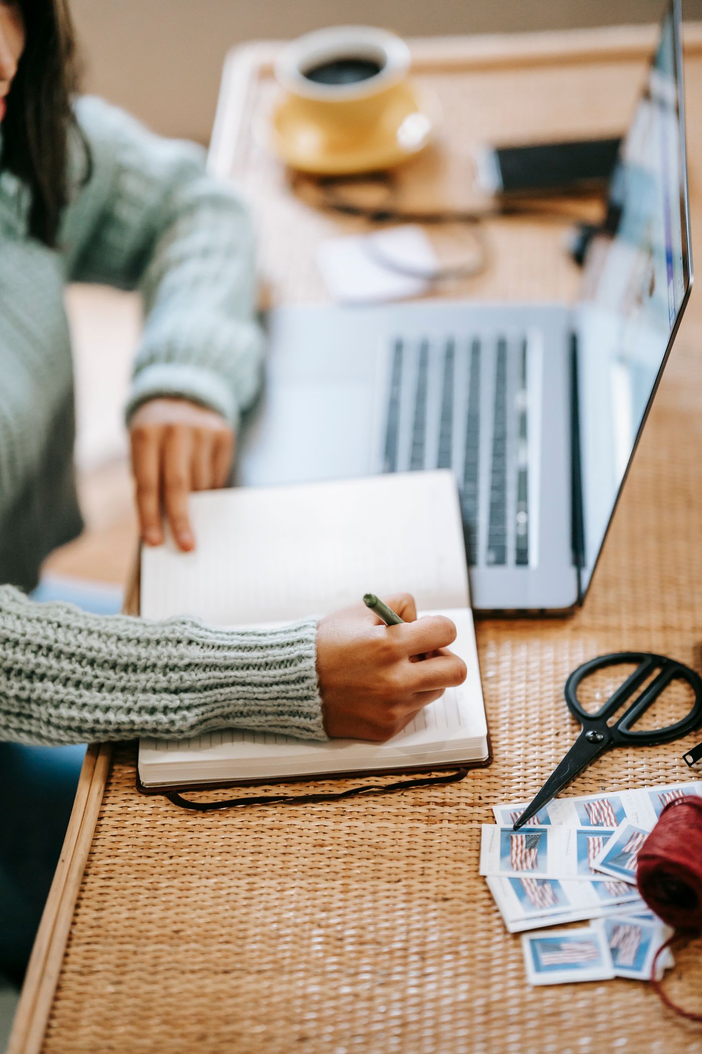 A woman taking notes beside a laptop and a cup of coffee