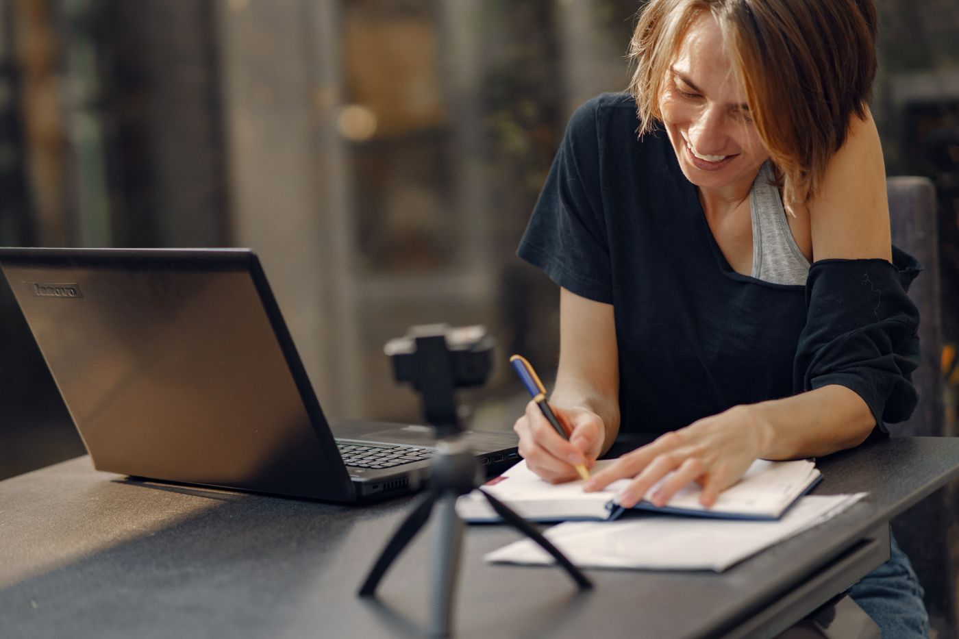 A woman smiling while writing notes beside a laptop