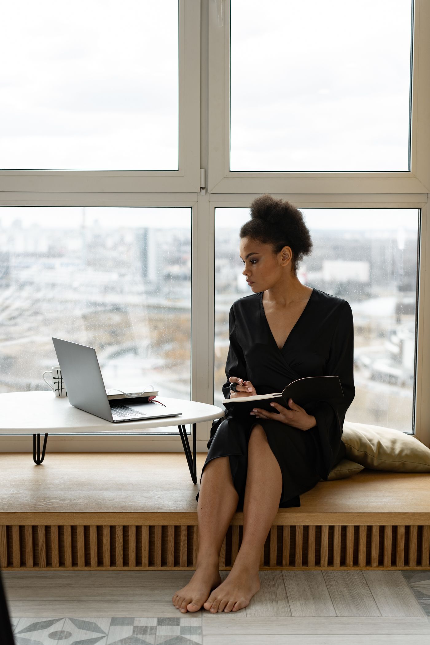 A woman working with a laptop and notebook by a window